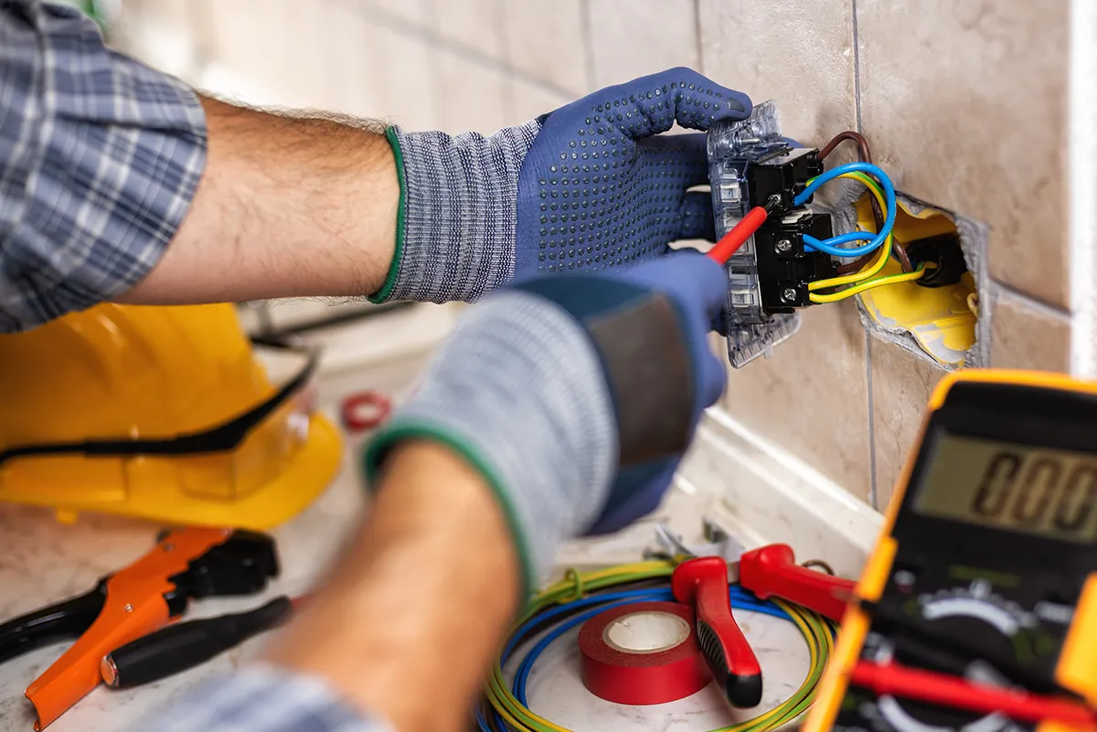Electrician with safety gloves repairing a wall socket and electrical wiring